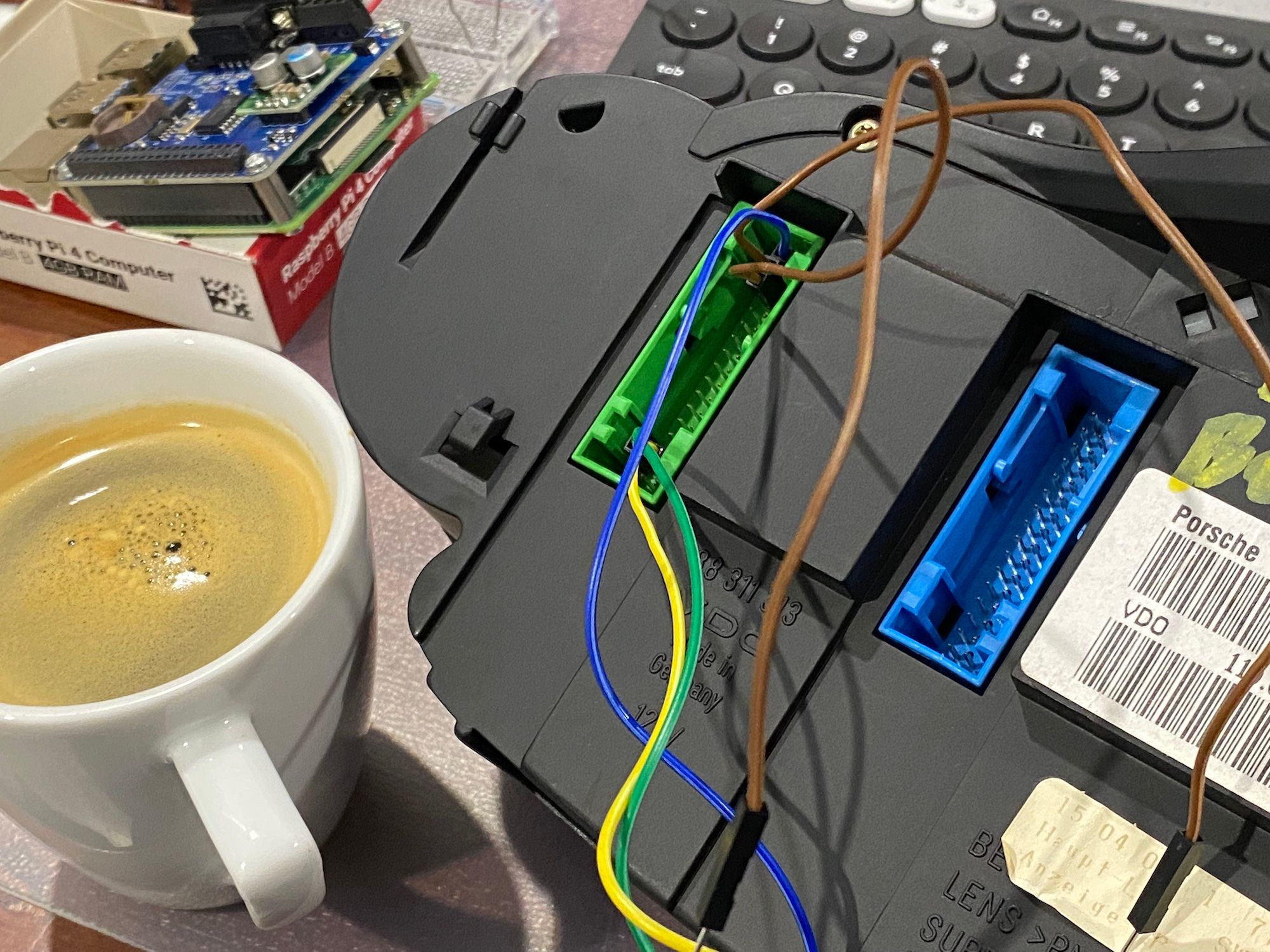 Raspberry Pi4 with PICAN3 hat, back of car instrument cluster with wires attached, keyboard and a coffee cup